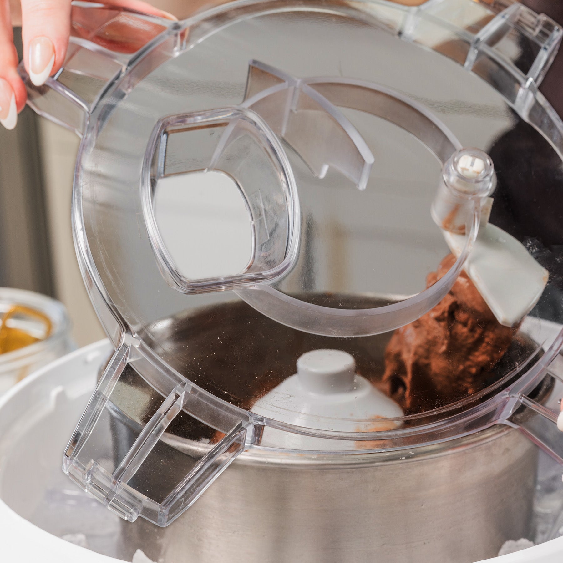 Close-up of a white ice cream maker with a clear lid churning chocolate ice cream