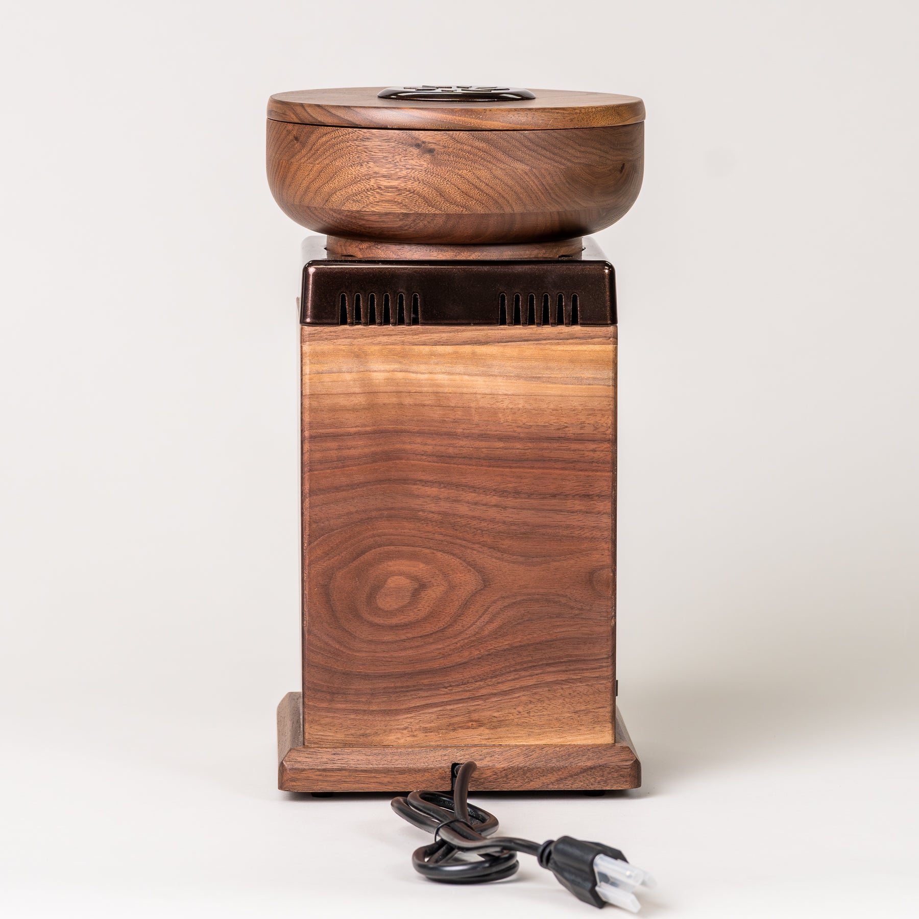 Behind angle of NutriMill harvest walnut grain mill with cocoa-colored trim and power cord on grey background