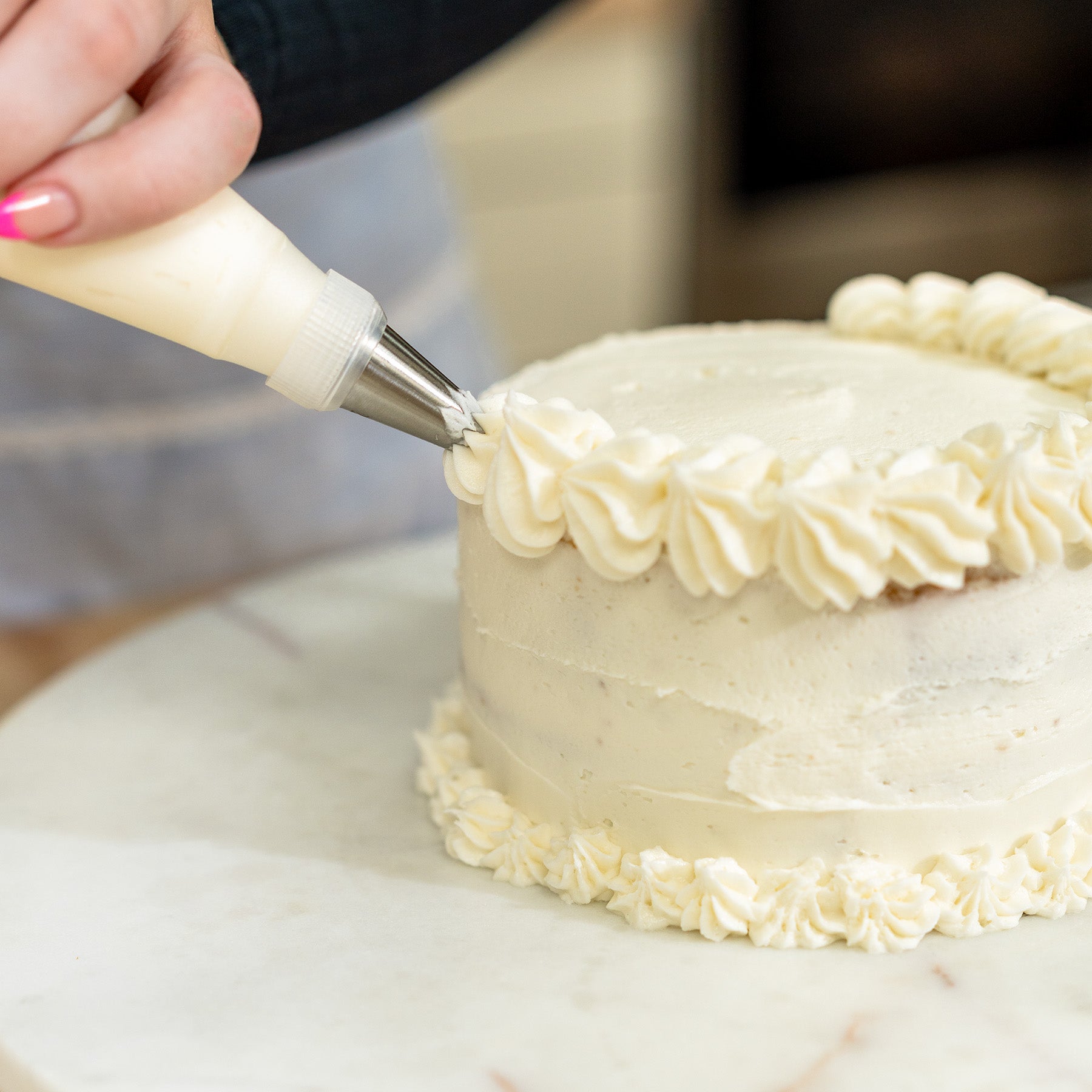 A woman icing a white cake with the NutriMill icing kit